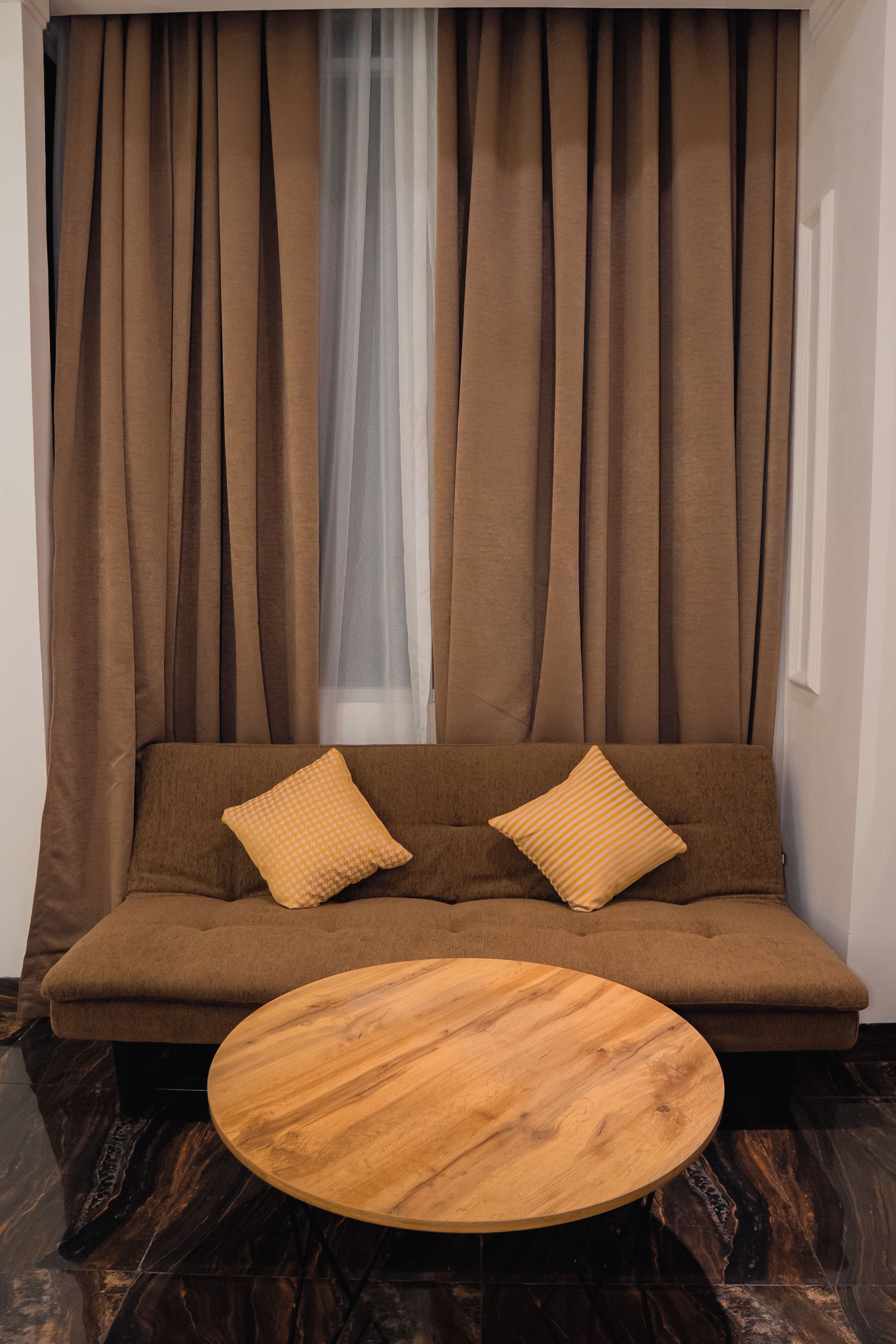 Uma sala de estar moderna com um sofá marrom, duas almofadas e uma mesa de centro redonda de madeira.