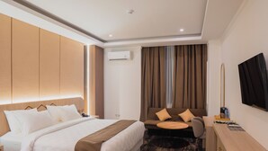 Una habitación de hotel con cama, sofá, escritorio, televisor y aire acondicionado.