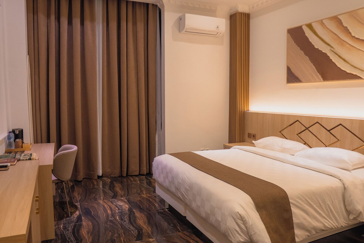 A hotel room with a bed, a desk, a chair, and a large window with curtains.