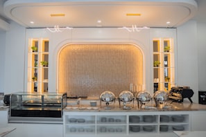 Uma mesa de buffet montada com diversas estações de serviço, vitrines de vidro e uma variedade de pratos.
