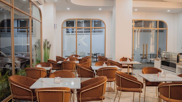 Interior moderno de restaurante con suelo de mármol, sillas tapizadas en tonos marrones y grandes ventanales con vistas a la calle.