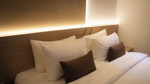 A neatly made bed with white and brown pillows, a wooden headboard, and a wall-mounted light fixture. - Fahira Hotel Syariah Padang (Padang)