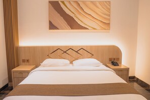 A hotel room with a large bed, a wooden headboard, a nightstand with a phone, and a wall-mounted artwork. - Fahira Hotel Syariah Padang (Padang)