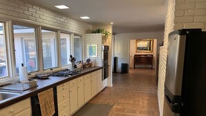 A kitchen with a brick wall backsplash, wooden cabinets, a stainless steel refrigerator, and a window overlooking a driveway.