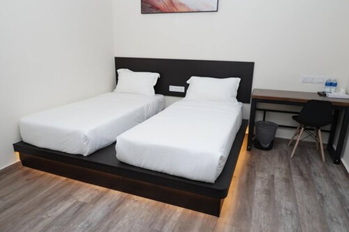 A modern hotel room with two single beds, a desk, and a chair.