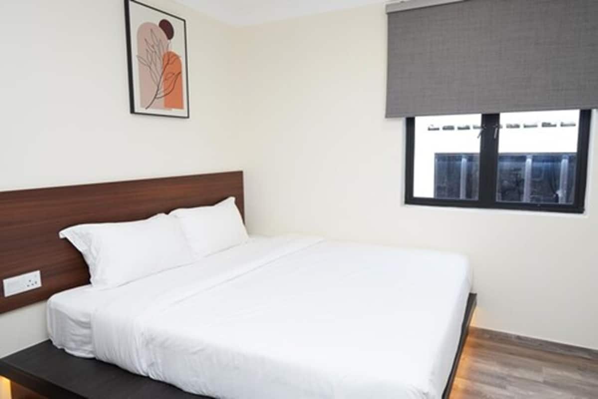 A neatly made bed in a room with a wooden headboard, a framed artwork on the wall, and a window with a view of buildings.