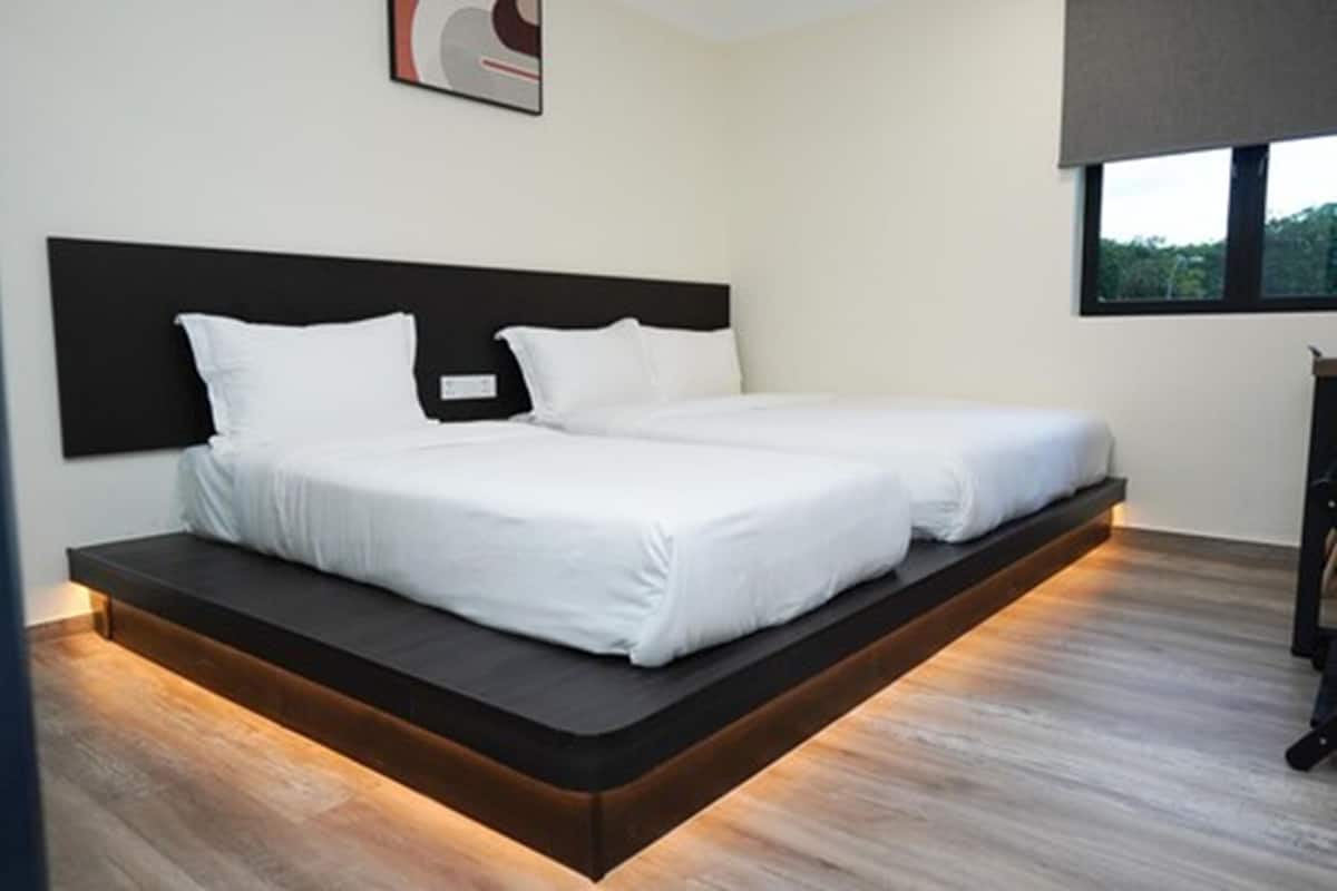 A modern bedroom with a bed that extends to the floor, a dark headboard, and a window with a view of greenery.