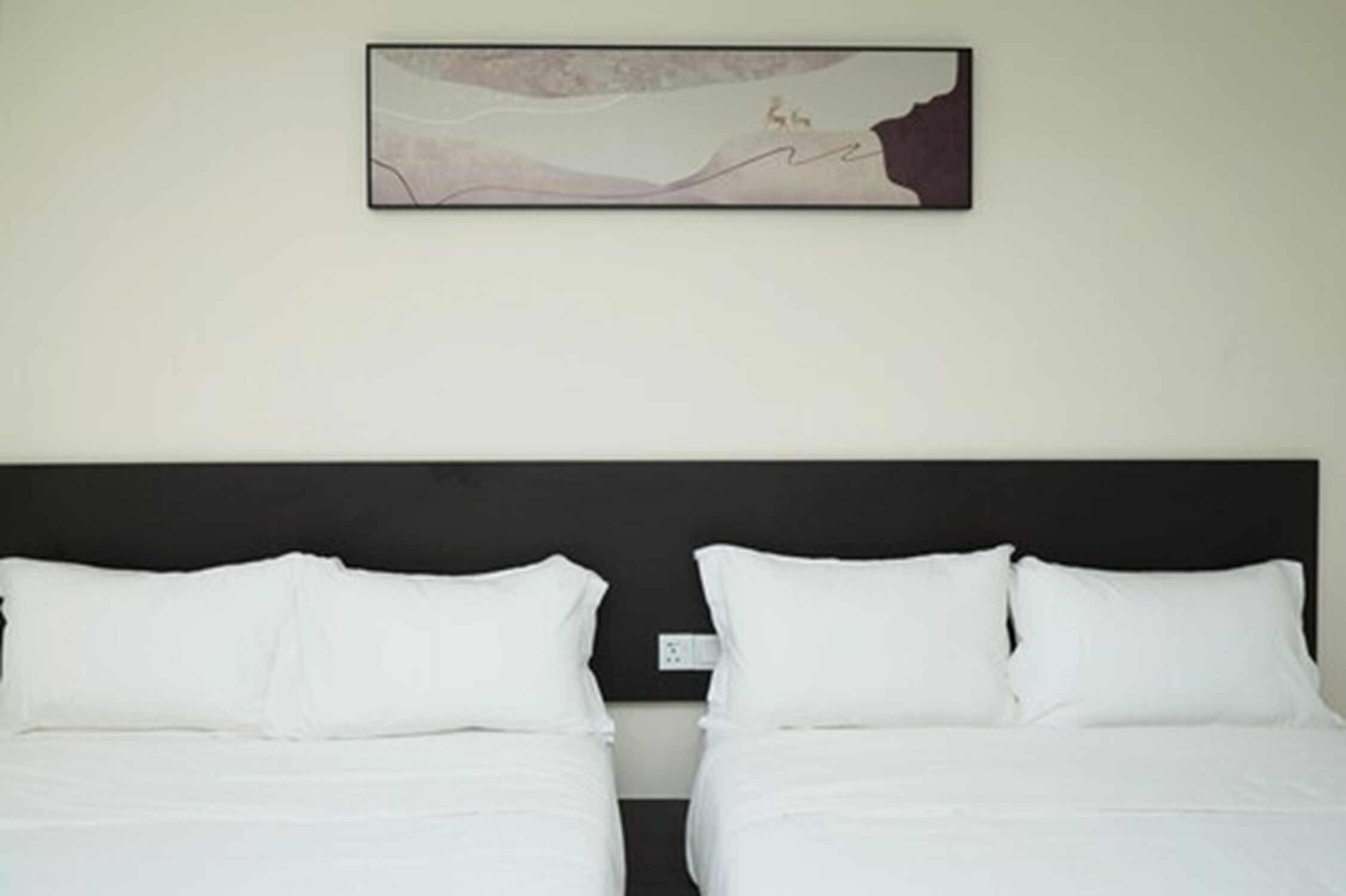 A hotel room with two beds, a dark headboard, and a wall-mounted abstract painting.