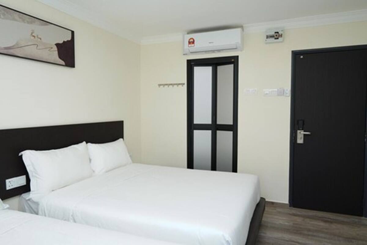A hotel room with two beds, a black door, and an air conditioning unit.