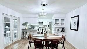 A spacious dining area with a wooden table and chairs, a kitchen in the background, and a framed picture on the wall.