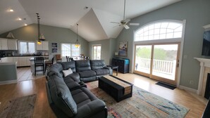 A spacious living area with a large L-shaped sectional sofa, a dining table with chairs, a kitchen area, and a balcony with a view. - Henry's Hideaway-Cape May- 2.5 blocks to beach- 5 BR- Elevator (Cape May)