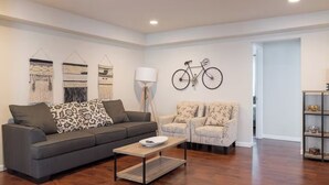 A modern living room with a grey sofa, patterned cushions, a coffee table, and a bicycle mounted on the wall.