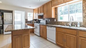 A modern kitchen with wooden cabinets, a granite countertop, a stove, and a dishwasher.