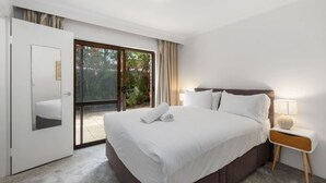 Ein Hotelzimmer mit einem großen Bett, einem Nachttisch mit Lampe und einer Glastür, die auf einen Balkon führt.