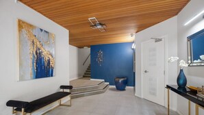 Ein modernes Interieur mit Holzboden, einer blauen Akzentwand, einem großen abstrakten Gemälde, einer Bank, einer Vase und einer Treppe.