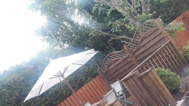 A patio area with a wooden fence, a white umbrella, and a planter with plants.