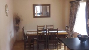 A dining area with a wooden table and chairs, a kitchen counter, and a mirror on the wall.