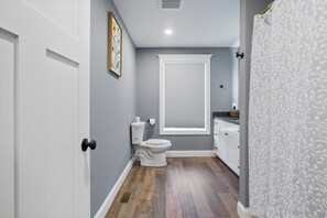 A bathroom with a toilet, a window with blinds, a sink, and a shower curtain. - Cool New Dover Home (Dover)