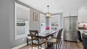 A modern kitchen with a large stainless steel refrigerator, wooden dining table with chairs, and a hanging light fixture. - Cool New Dover Home (Dover)