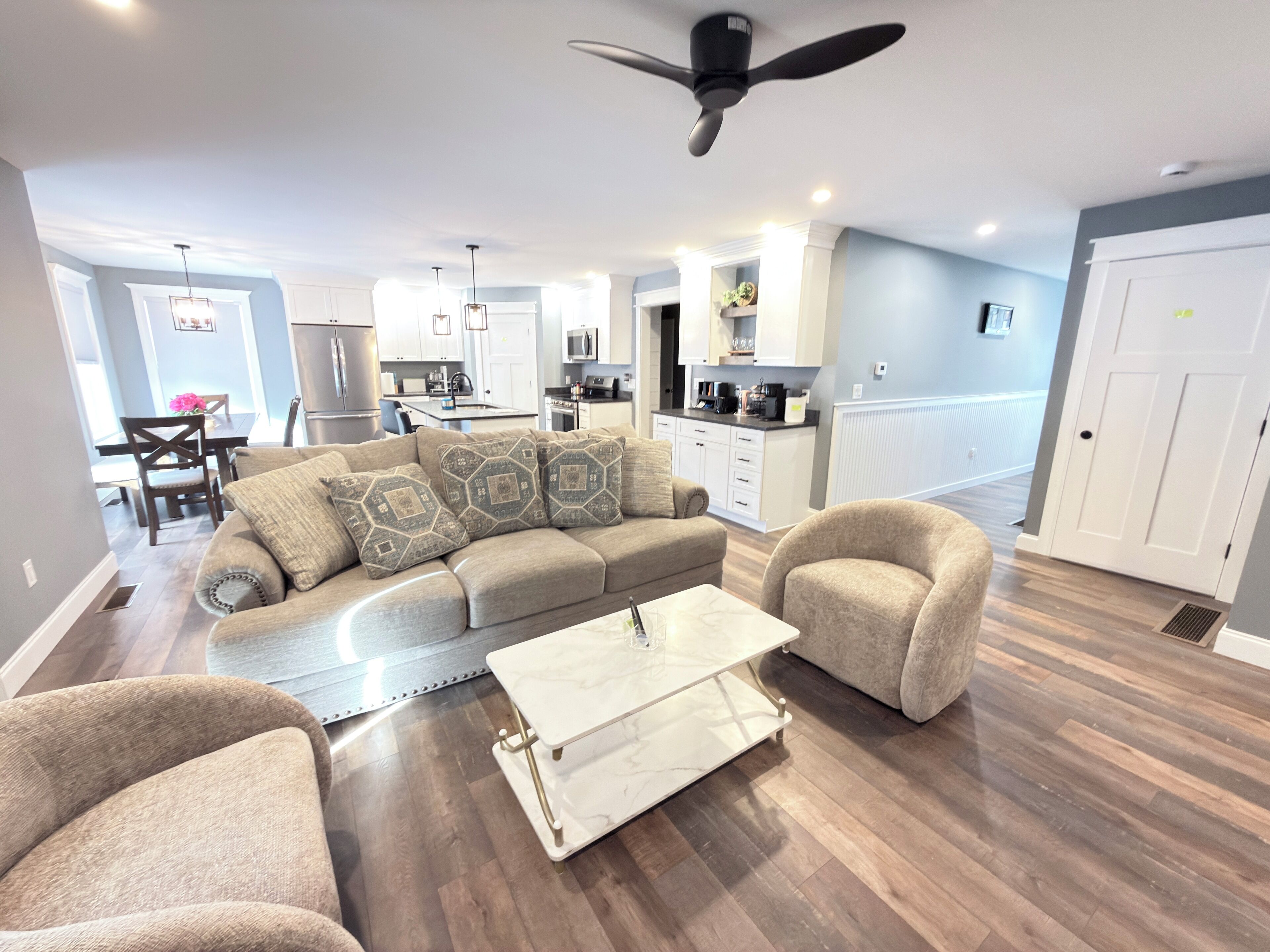 Una sala de estar moderna con un sofá modular, una mesa de centro y dos sillones. Se puede ver una cocina y un comedor al fondo.