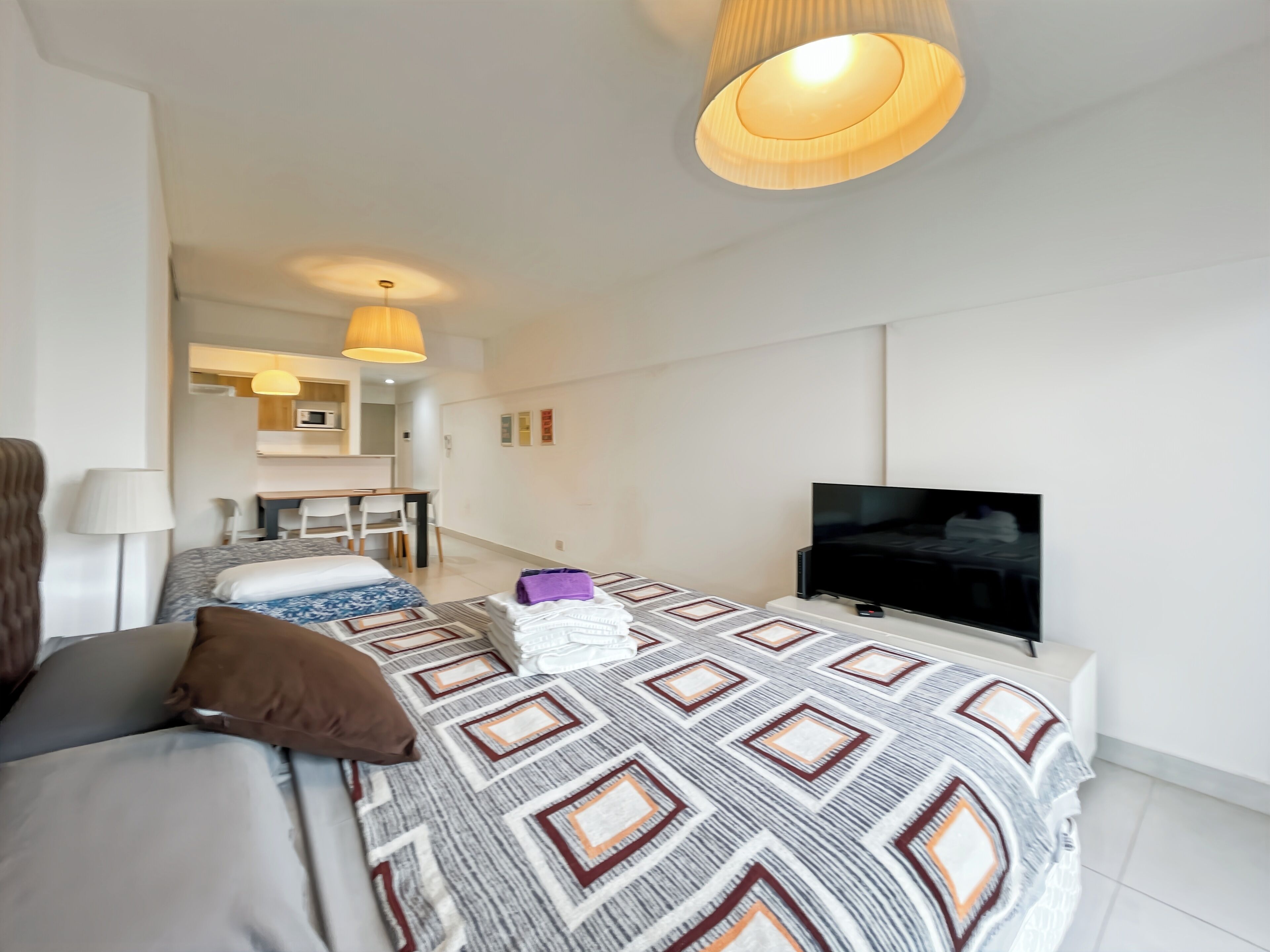 A modern hotel room with a large bed, a TV, a desk, and a kitchenette.