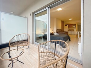 A modern hotel room with a balcony, wicker chairs, a bed, a desk, and a kitchenette. - Ayres Suites Rio de Janeiro (Buenos Aires)