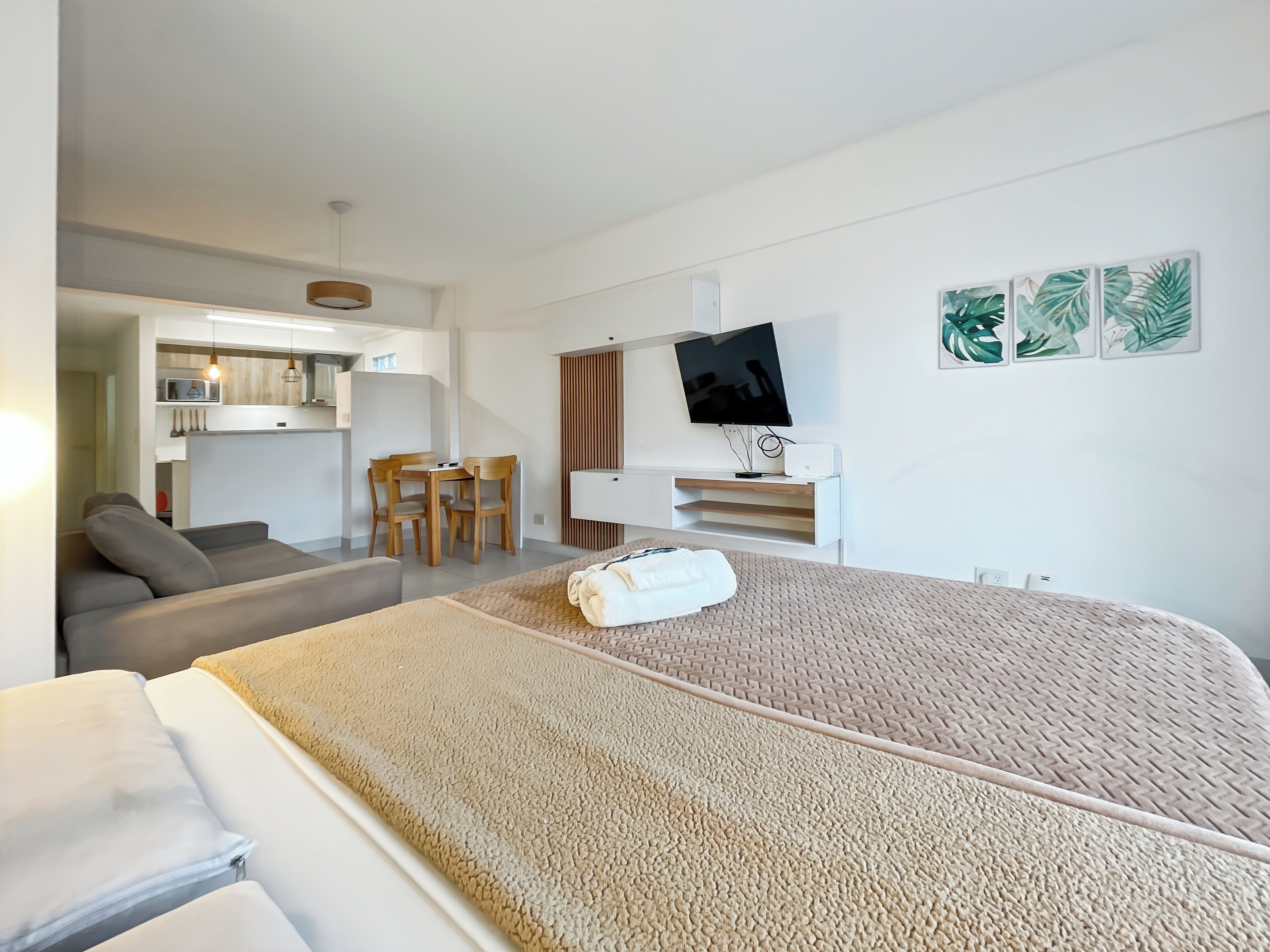 A modern hotel room with a bed, a sofa, a dining table with chairs, a TV, and artwork on the wall.