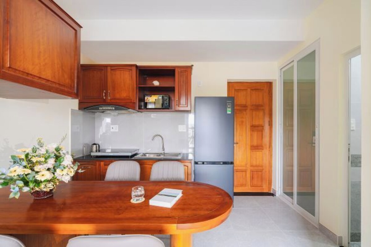 A modern kitchen with wooden cabinets, a stainless steel refrigerator, and a dining table with chairs.