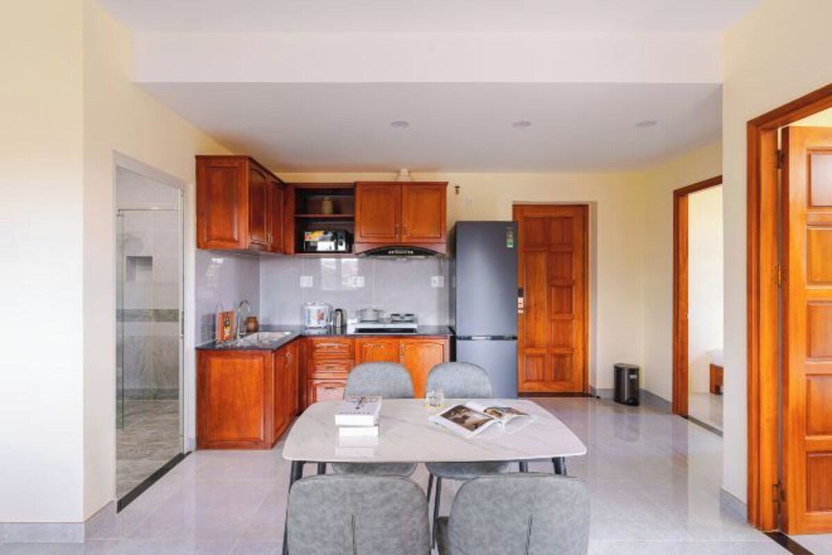 A modern kitchen with wooden cabinets, a refrigerator, and a dining area with a table and chairs.
