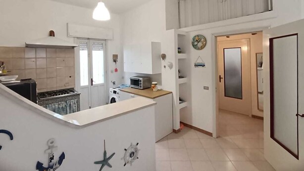 A compact kitchen with a central island, a washing machine, and a dining area with a view of the living room. - Villa Iris with large veranda (San Pietro In Bevagna)
