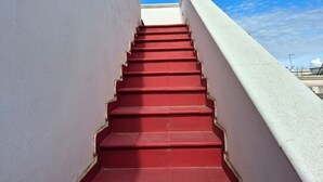 A set of red stairs leading upwards, flanked by white walls, under a clear blue sky. - Villa Iris with large veranda (San Pietro In Bevagna)