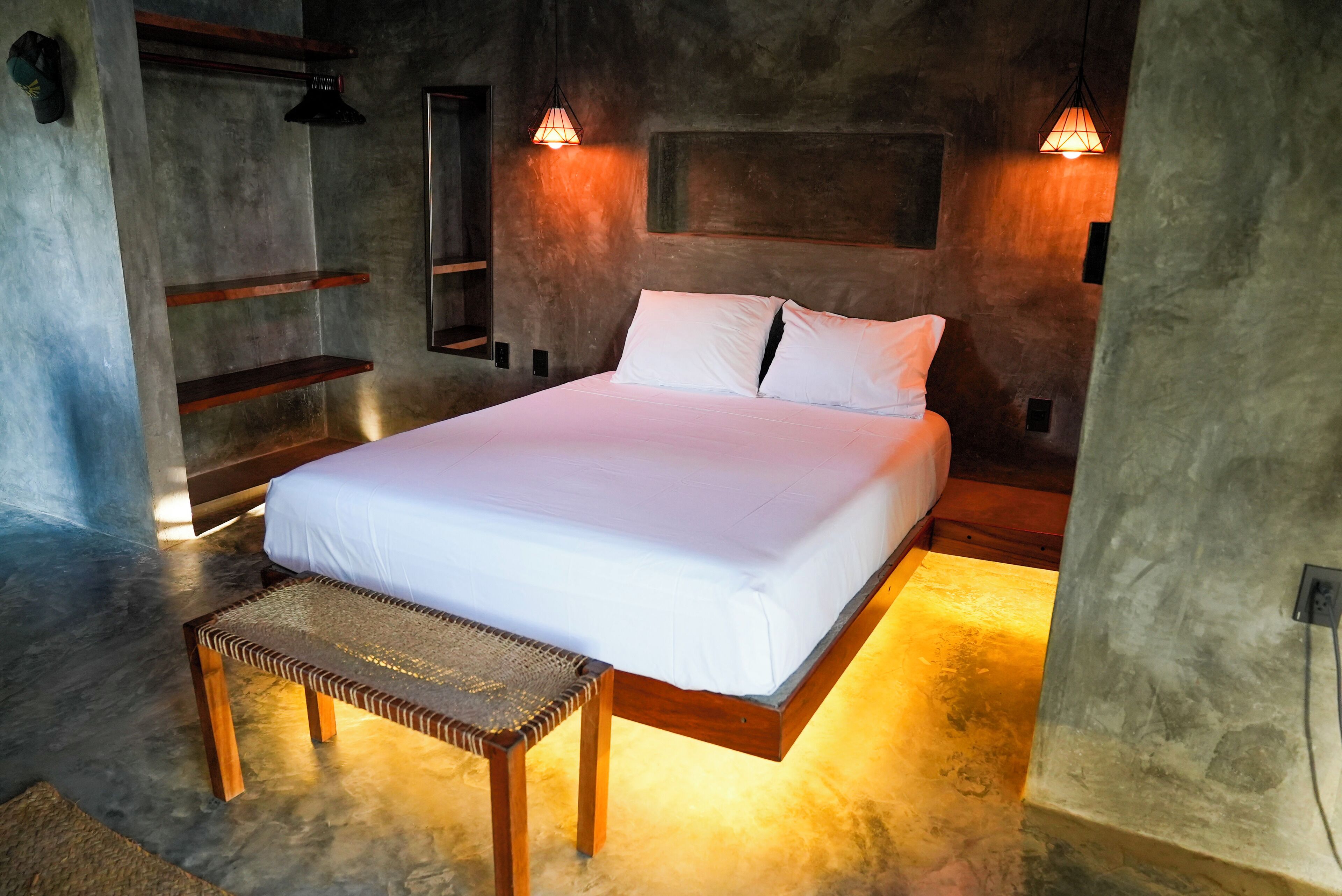 Un dormitorio con una cama, un banco y dos luces fijadas a la pared.