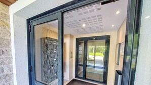 Une entrée moderne avec des portes en verre, un mur en pierre et un plafond doté d’un éclairage encastré.