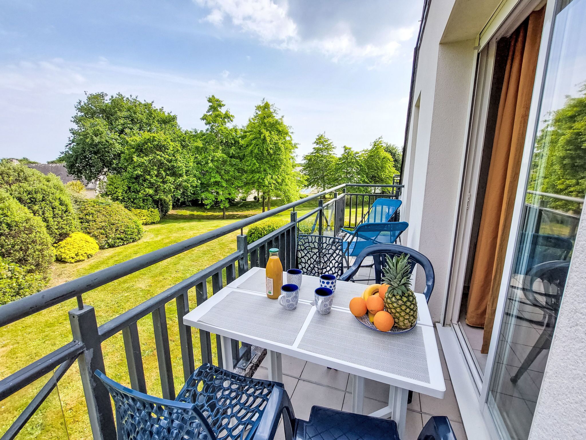 A balcony with a table set for two, a pineapple, and a bottle of orange juice.