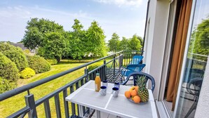 Un balcon avec une table dressée pour deux personnes, un ananas et une bouteille de jus d’orange.