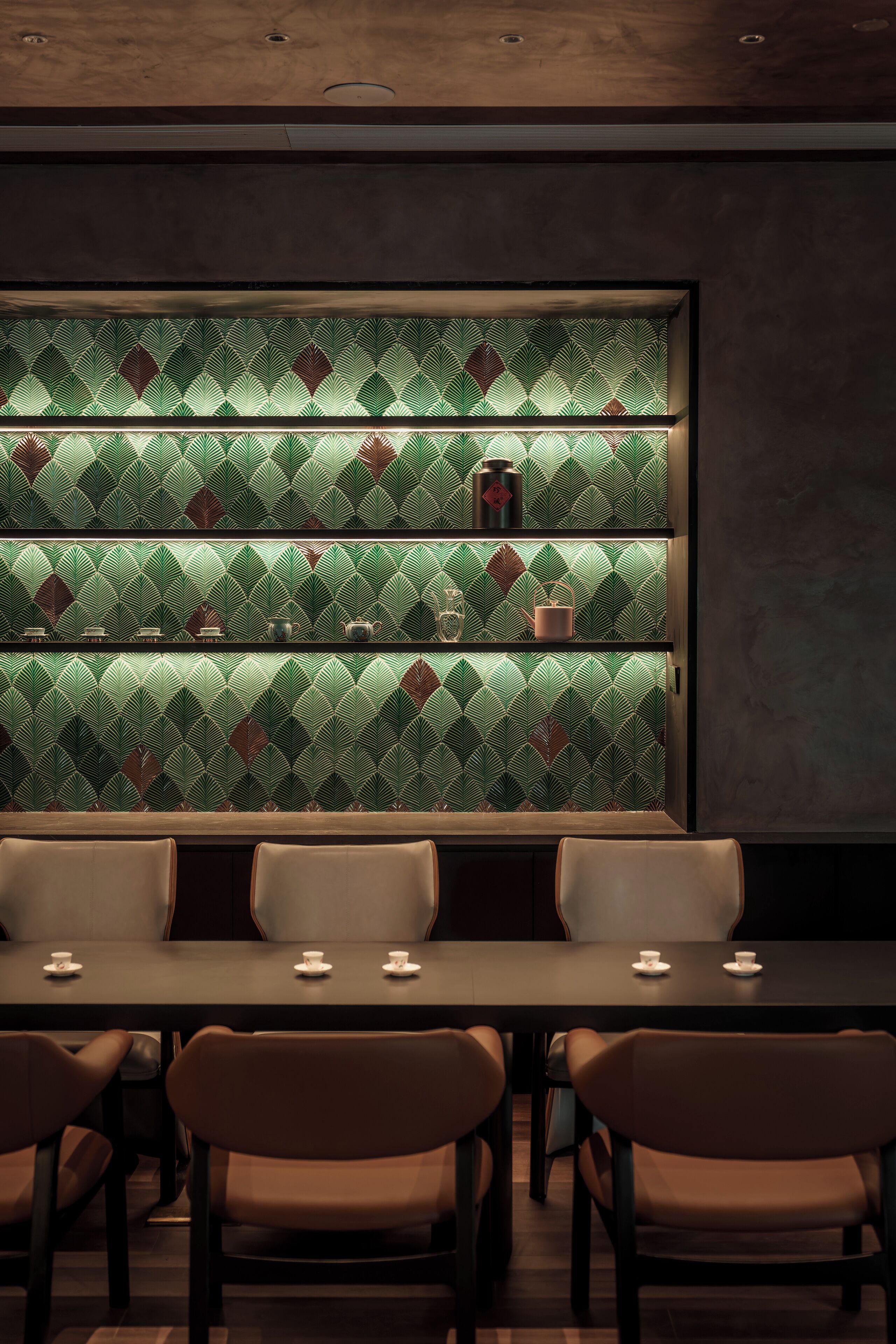 Un espace repas comprenant une longue table et plusieurs chaises, un mur orné d’un motif derrière la table, et des étagères où sont disposés des objets décoratifs.