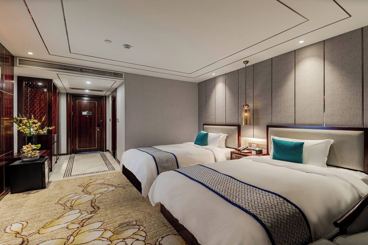 A hotel room with two beds, a large mirror, a nightstand, a desk, and a decorative vase with flowers.
