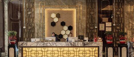 A reception desk with a marble top, geometric wall design, and potted plants.