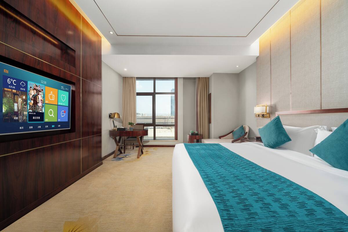A hotel room with a large bed, a desk, a television, and a window with curtains.