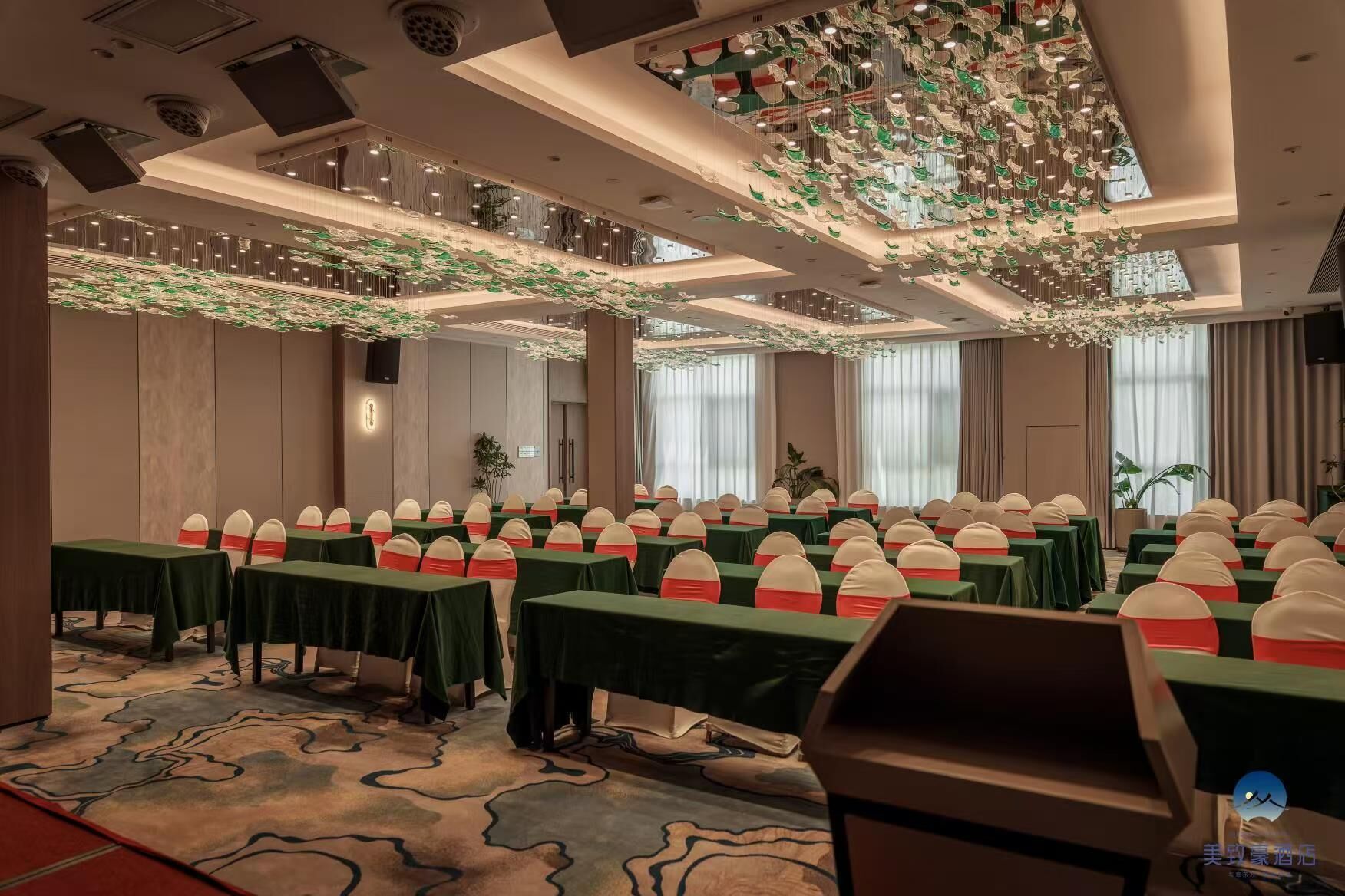A conference room with rows of tables, green tablecloths, and chairs with red sashes.