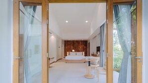 A modern bedroom with a large bed, bedside tables, and a view of greenery through the window. - Baan phandao (Rim Nuea)