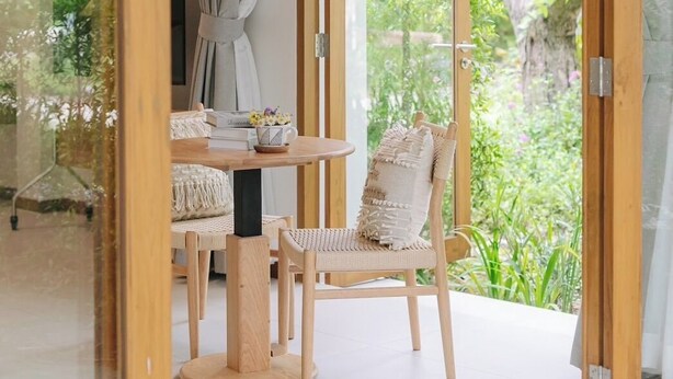 A room with a glass door leading to a garden, a round wooden table with chairs, and a view of greenery outside. - Baan phandao (Rim Nuea)