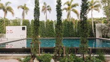 A swimming pool with a clear blue water, surrounded by tall palm trees and a white wall with a lifebuoy decoration.