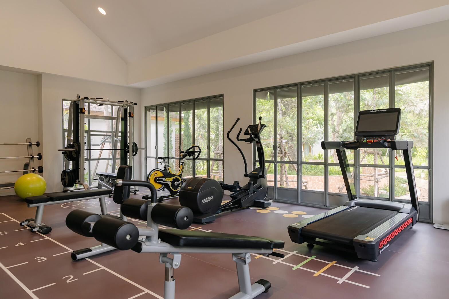 A gym with various exercise equipment, large windows, and a clear view of the outdoors.
