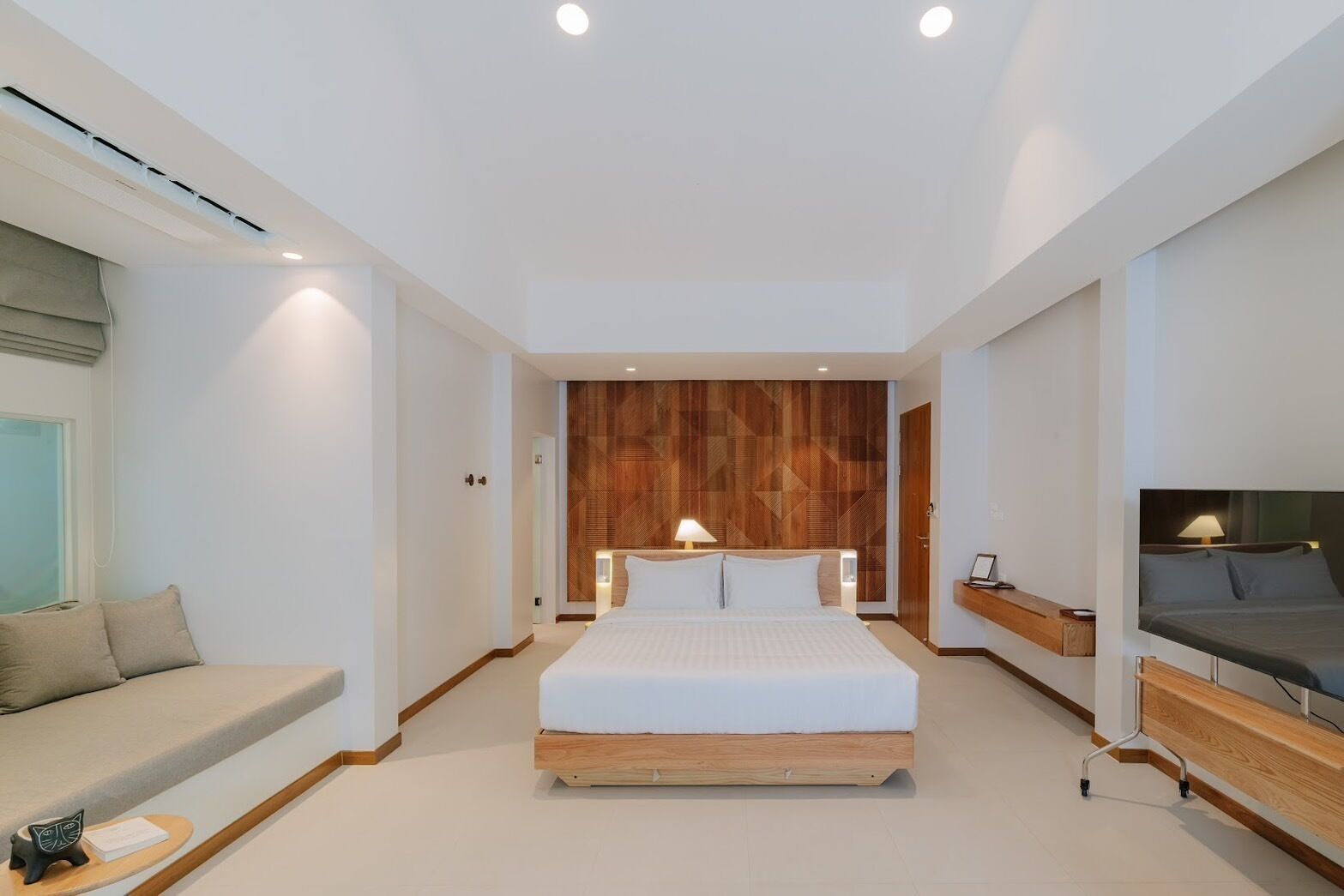 A modern hotel room with a large bed, a sofa, a TV, and a wooden accent wall.
