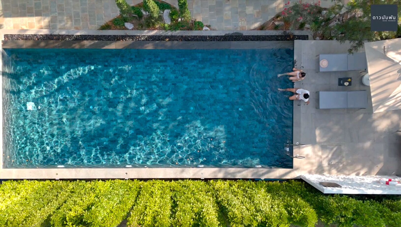 Una piscina rectangular con agua azul cristalina, rodeada por un borde de baldosas y abundante césped verde.