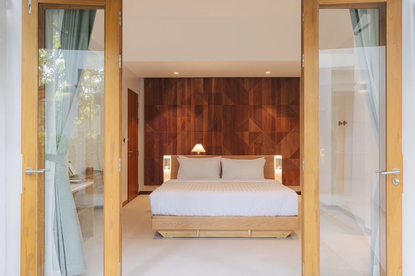 A modern bedroom with a wooden headboard, a bed with white linens, and a bedside lamp.
