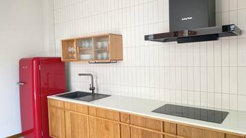 Una cocina con un refrigerador rojo, armarios de madera, una encimera blanca, un lavamanos negro y una campana extractora negra.