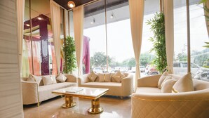 A spacious lounge area with two sofas and a coffee table, large windows with sheer curtains, and a view of the street outside.