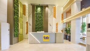 A modern hotel reception area with a reception desk, green vertical garden, marble walls, and a clean, polished floor.